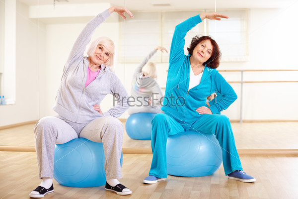 Portrait of sporty females doing physical exercise on balls in sport gym