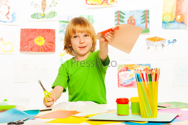 Blond happy boy with scissors and paper cutting paper on craft lesson, stock photo