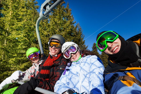 Happy snowboarders sitting together wearing ski masks in elevator in mountains and forest area, stock photo