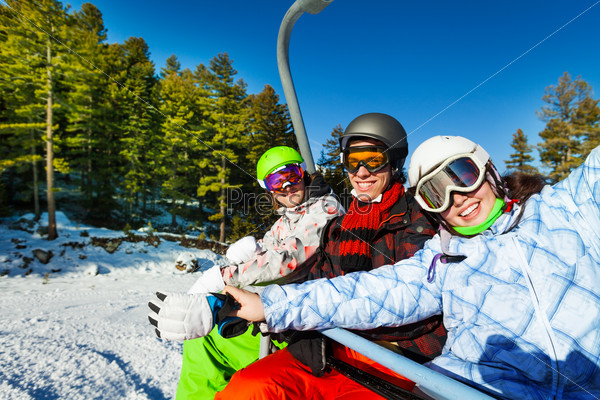 Three happy snowboarders in ski masks sitting together in elevator in mountains and forest area