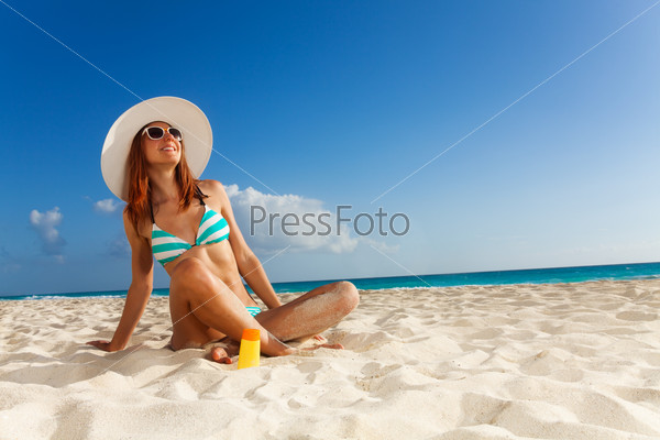 Красивая женщина в купальнике и шляпе позирует на белом песчаном пляже