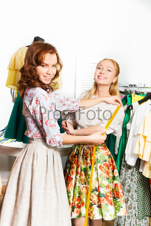 Two happy women measure size of the skirt in shop