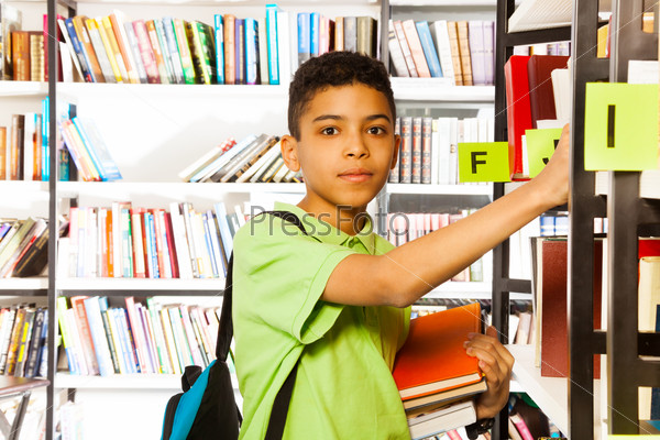 Serious boy looks and searches book on shelf
