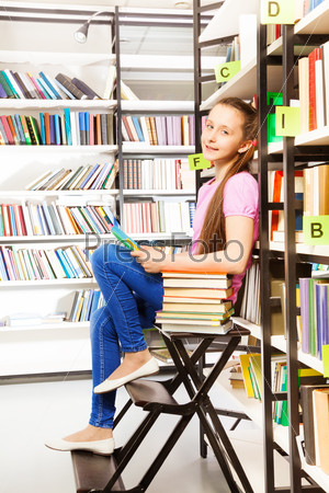Smiling girl sitting on step ladder in library