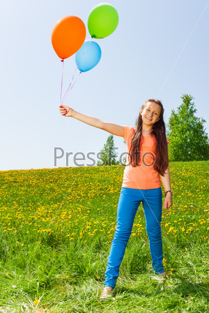 Smiling girl holding three balloons in summer