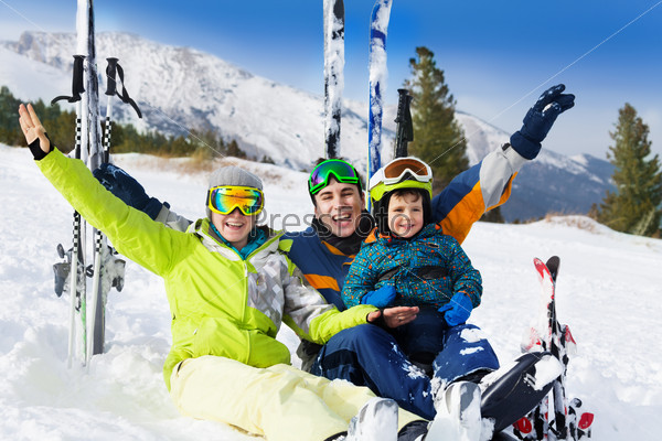 Happy family with hands up on snow after skiing