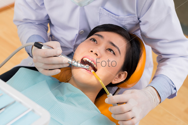 Dentist drilling tooth of a young woman, view from above