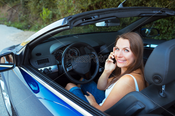 Smiling caucasian woman talking on phone in a cabriolet car