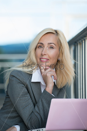 Beautiful business woman smiling while working on laptop near her office outdoor