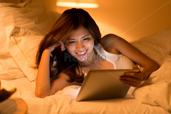 Young smiling woman watching movie on the digital tablet at night
