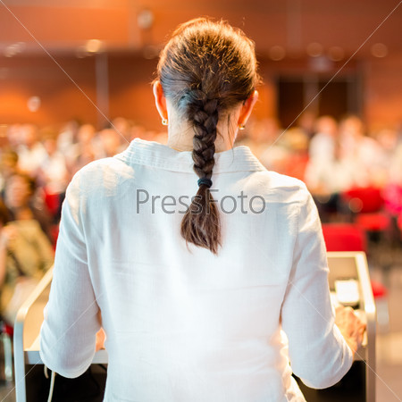 Female academic professor lecturing at Conference. Audience at the lecture hall.