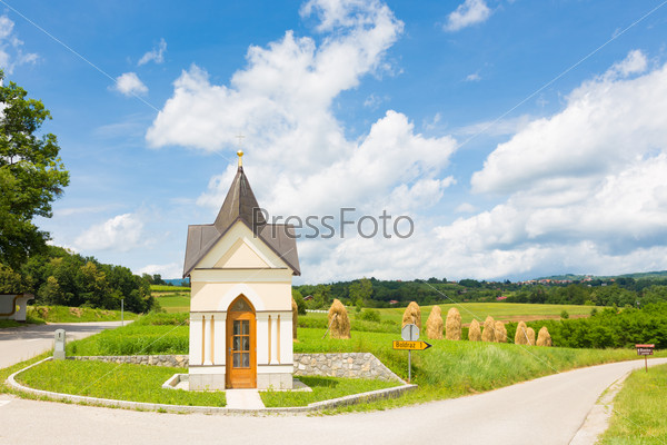 Bela krajina, Slovenia. Traditional christian chapel and hay stacks on the field in the background.