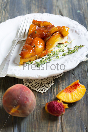 Plate with peach pie and thyme on a wooden table.