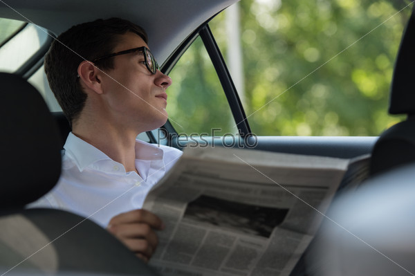 Businessman in car reading newspaper