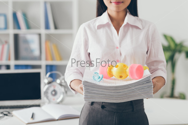 Cropped image of business woman holding stack of documents and baby toys on the top of it
