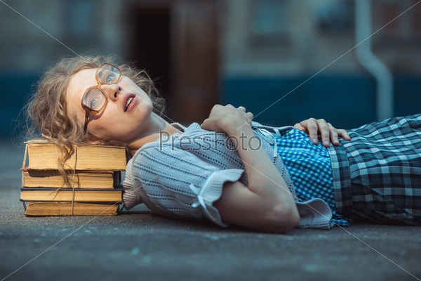 Funny crazy girl student with glasses lying on a pile of books outdoor
