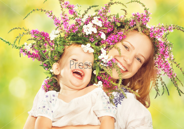 happy laughing family, daughter hugging mother in wreaths of summer flowers in nature