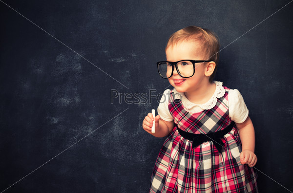 funny baby girl pupil in glasses and chalk at a school board