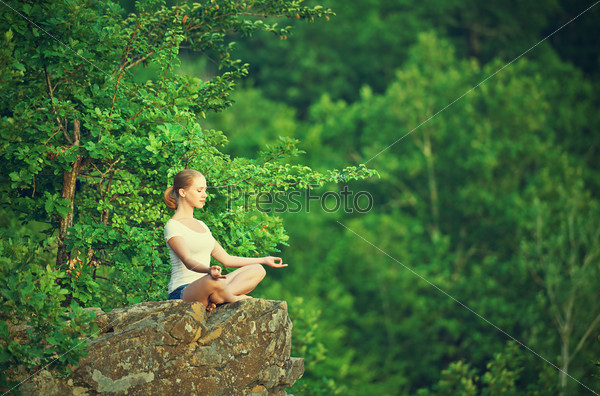 woman meditating in lotus posture, doing yoga on top of the mountain on a rock in nature in the forest