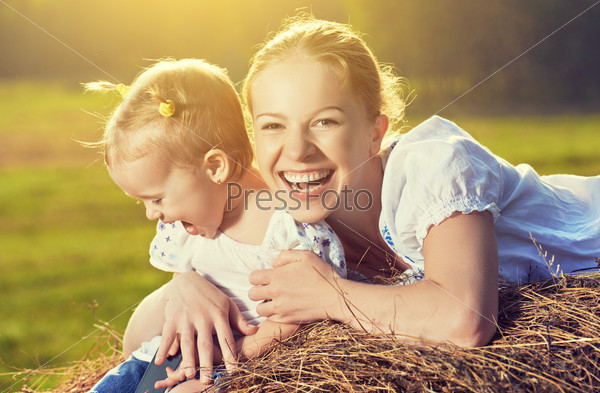 happy family in summer nature. Mother and baby daughter laugh, hug, play in the hay, straw.