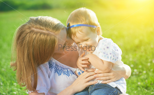 Happy family on nature outdoors mother tickle baby daughter and laugh on the green meadow , stock photo