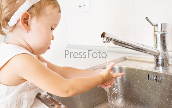 Baby girl washes her hands in the bathroom with running water, stock photo