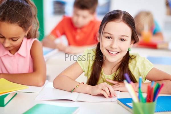 Happy little girl looking at camera at lesson with her friend near by