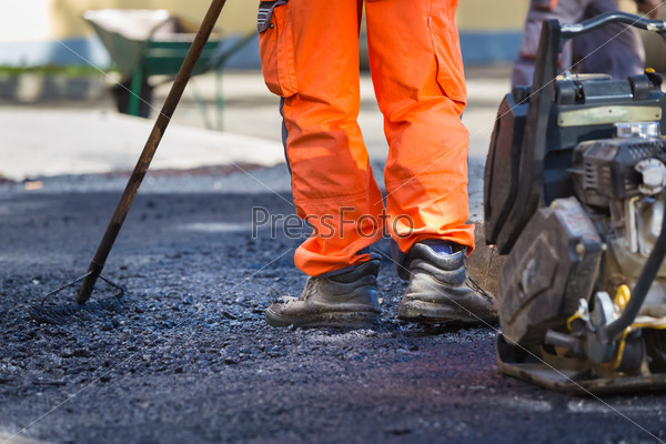 Construction workers during asphalting road works wearing coveralls. Manual labor on construction site, stock photo