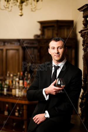 Attractive man in tuxedo having a glass of cognac. See more images from the same shoot.