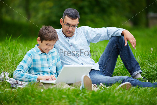 Young man and his son using laptop while relaxing in the park