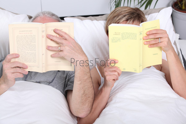 Couple reading together in bed, stock photo