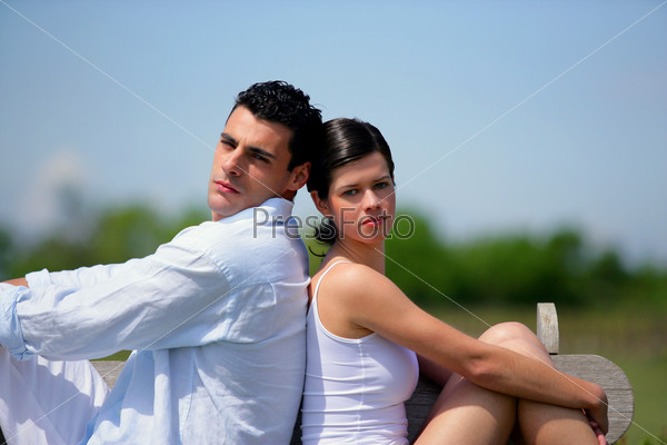 Young couple sat back to back on bench, stock photo