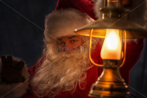 Santa Clause walking outdoors under falling snow with vintage lamp