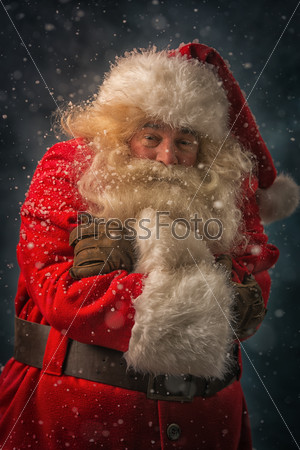 Santa Claus is feeling very cold standing outdoors at snowfall at north pole with hands folded