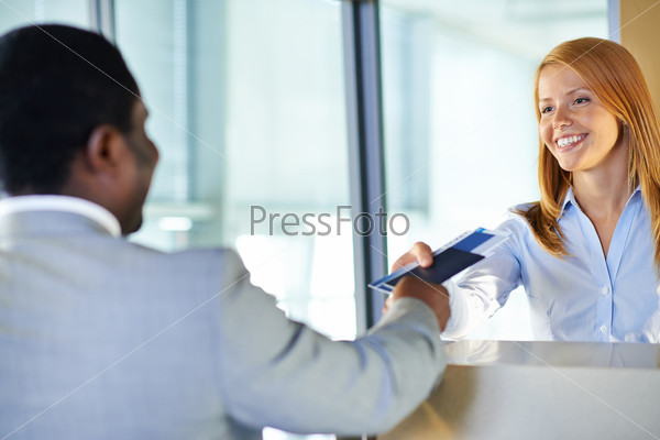 Attractive young woman giving passport and ticket back to businessman at airport check-in counter