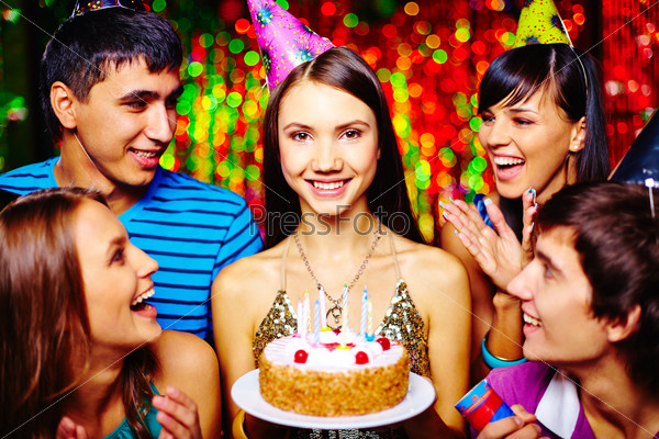 Attractive girl with birthday cake and her friends having party