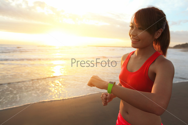 Health sport young woman run and look wear smart watch device with touchscreen on the beach at sunrise, asian