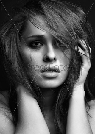 Young pretty woman with smeared mascara crying on black background
