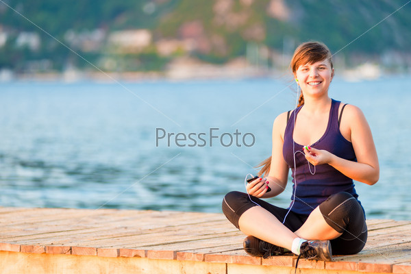 funny and beautiful girl with headphones sitting on the pier\
in the morning