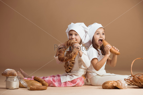 Two 5 years old girl bakers eating bakery products, studio shot