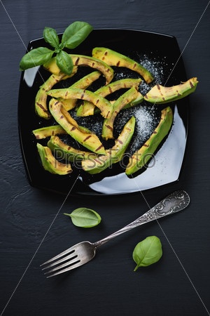 Grilled avocado slices with sea salt on black, view from above