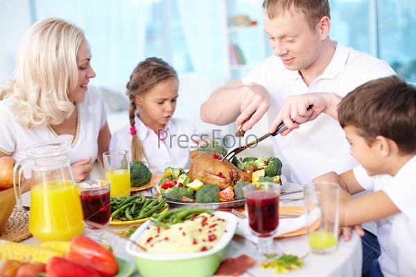 Modern family sitting at festive table and going to eat roasted turkey, young man cutting it
