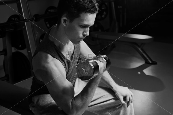 Black-and-white image of handsome man training in gym with dumbbell , stock photo