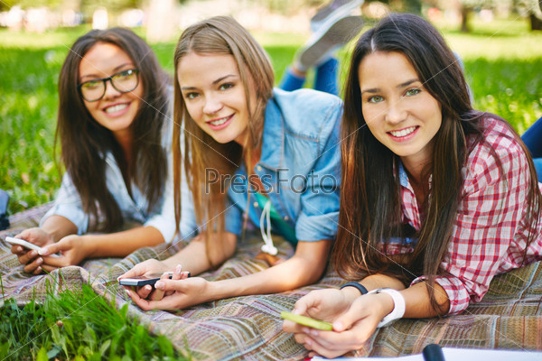 Positive teenage girls with telecommunication technologies looking at camera in park