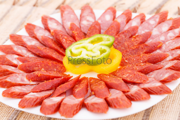 Fresh sausages and peppers in plate on bamboo mat background.