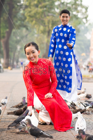 Lovely Vietnamese couple in traditional clothes feeding pigeons