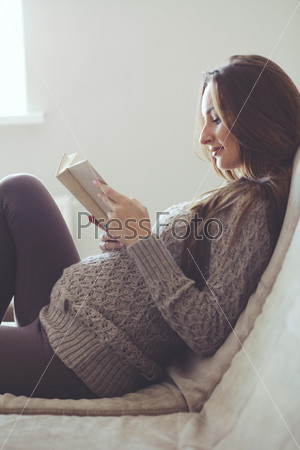 Home cozy portrait of pregnant woman resting at home and reading book on sofa