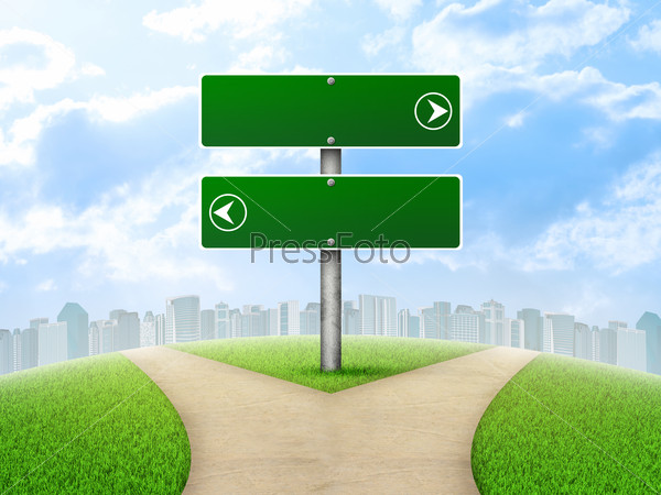 Crossroads road sign. City, green grass, fork in the way and sky as backdrop