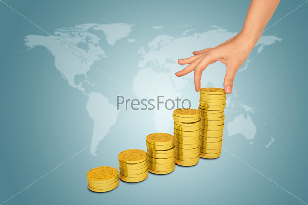 Female hand puts coin on pile of coins. World map on background