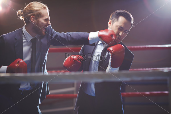 Powerful businessman in suit and boxing gloves attacking his rival